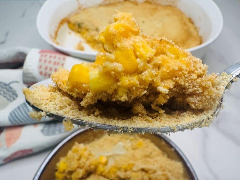 A spoonful of golden corn casserole being lifted from a baking dish.