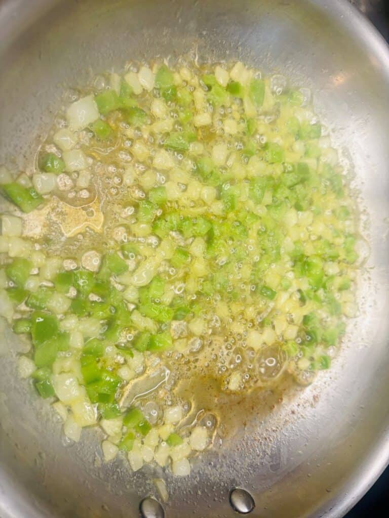 Finely diced green bell peppers and onions sautéing in a metal pan.