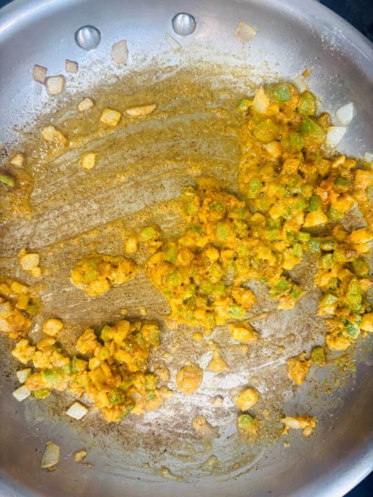 Sautéed diced green peppers and onions coated in yellow spices in a stainless steel skillet.