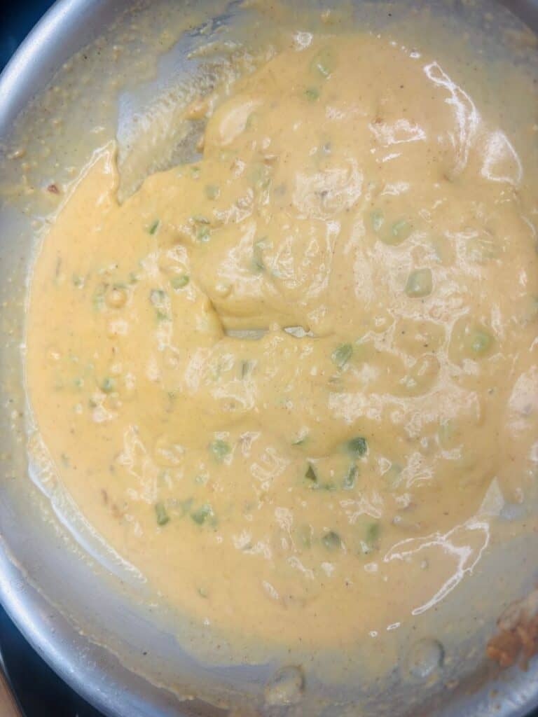 A creamy orange cheese sauce with bits of green peppers in a metal pan.