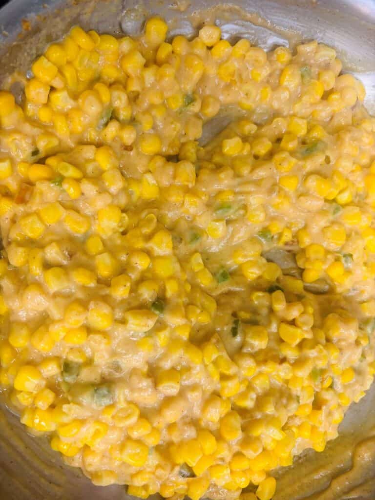 Creamy corn with small pieces of green peppers in a metal pan.