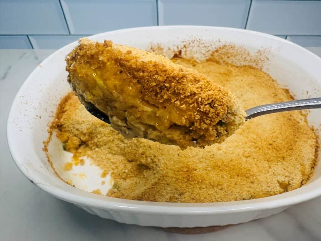 A spoonful of baked casserole with a golden, breadcrumb-crusted top being lifted from a ceramic baking dish.
